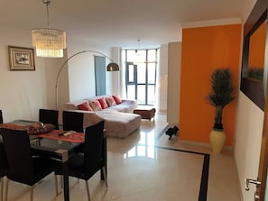 A modern living room with a sofa, dining table, chairs, and a large window. - Luxury Apartment, Near Beach&golf (Seixal)