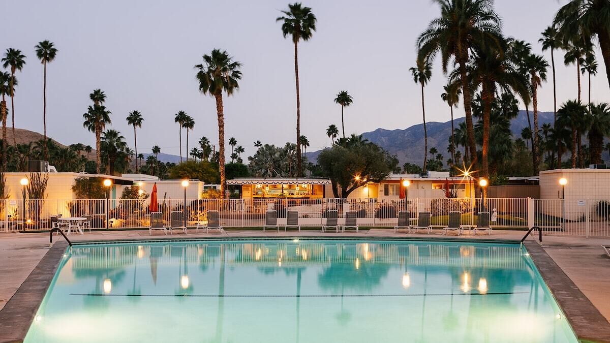 A swimming pool with lounge chairs and umbrellas, surrounded by palm trees and a mountain in the background.