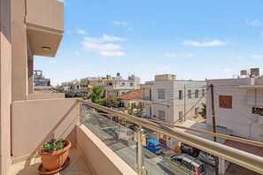 Uma varanda com um vaso de planta, com vista para uma rua com carros estacionados e edifícios ao fundo.