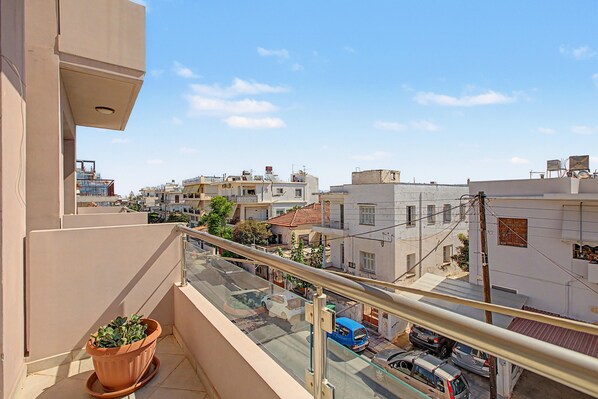A balcony with a potted plant, overlooking a street with parked cars and buildings in the background. - Apartment 'Happiness in Chania' with Wi-Fi (Chania)