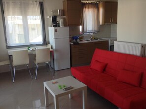 A compact living space with a kitchenette, a dining area with a table and chairs, and a red sofa. - Apartment 'Happiness in Chania' with Wi-Fi (Chania)