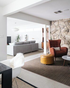 Ein modernes Wohnzimmer mit einem grauen Sofa, einem roten Sessel, einem runden Couchtisch und einer Steinwand.