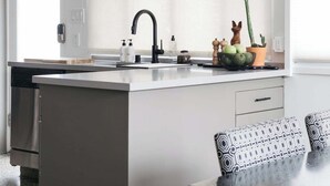 Eine moderne Küche mit einer zentralen Kochinsel, Pendelleuchten und einem Essbereich mit gemusterten Kissen.