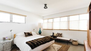 Ein Schlafzimmer mit Bett, Nachttischen, einer Lampe, einem Radio und einem Fenster.
