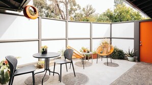 Eine Terrasse im Freien mit Sitzgelegenheit, darunter ein runder Tisch und Stühle, umgeben von Blumentöpfen.