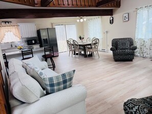 A living room with a sofa, a patterned armchair, a dining area with a table and chairs, a kitchen with a refrigerator, and a clock on the wall. - Family Escape with Loft and Fireplace. (Tobyhanna)