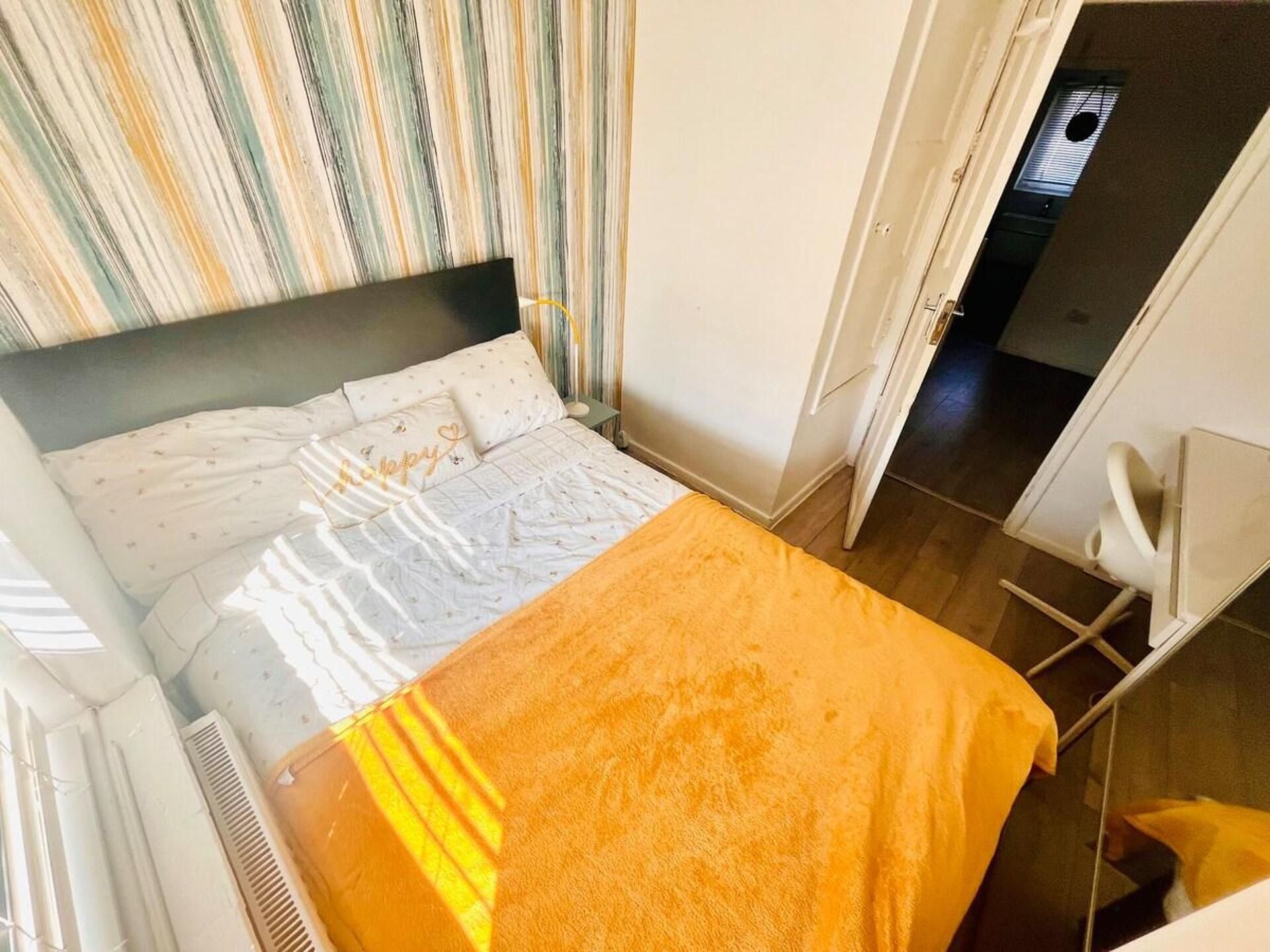 A bedroom with a bed, a bedside table, a chair, and a window with curtains.