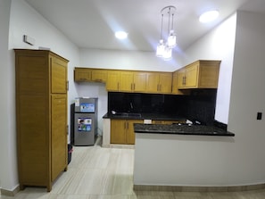 Eine Küche mit Holzausstattung, einem Kühlschrank, einer schwarzen Arbeitsplatte und einer Leuchte.