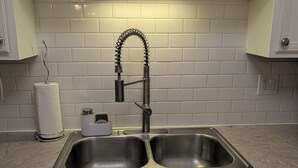 A kitchen with a double stainless steel sink, white cabinets, and a tiled backsplash.