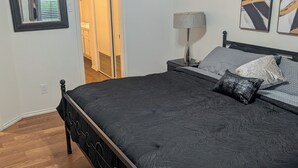 A bedroom with a bed, a nightstand, a lamp, a ceiling fan, a door, and a window.