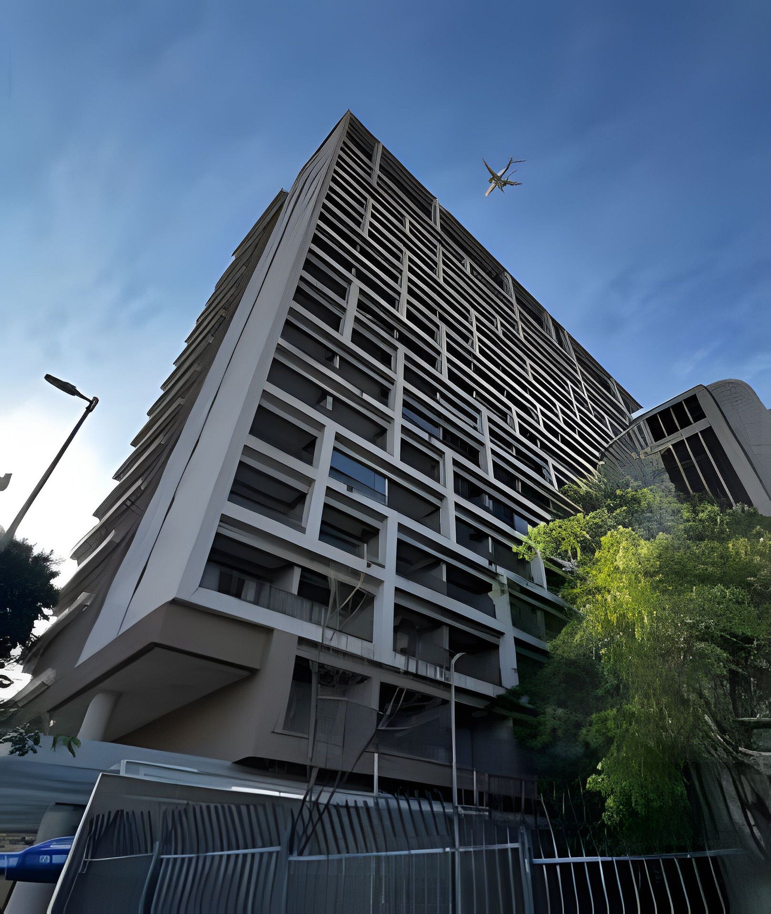 Un bâtiment moderne et imposant, doté d’une façade à motifs géométriques, un lampadaire et un arbre au premier plan.