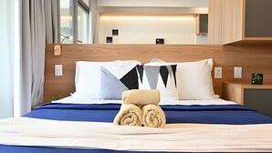 Een moderne hotelkamer met een houten hoofdeinde, een opgemaakt bed met een blauwe sprei, en uitzicht op het interieur van de kamer.