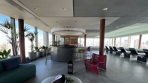Een ruime lobby met een bar in het midden, zitgedeeltes en grote ramen met uitzicht over de stad.