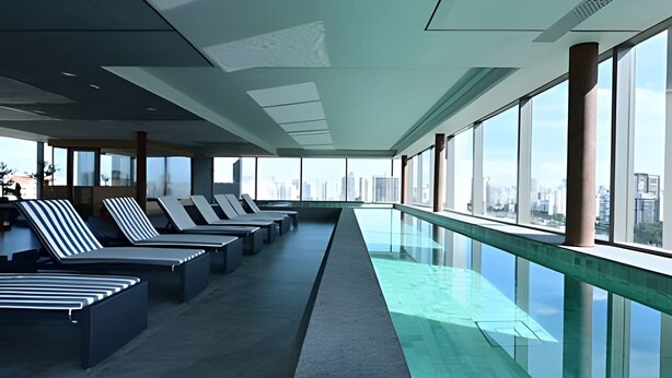 Een moderne hotellobby met een lange receptiebalie, lounge fauteuils en een glazen balustrade met uitzicht op een stadsbeeld.