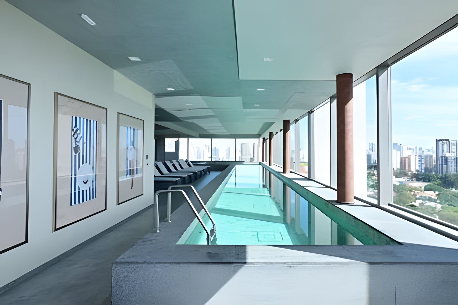 Una piscina interior moderna con vistas a la ciudad, zona de estar y cuadros enmarcados en las paredes.