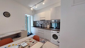 Cocina compacta con lavadora, horno empotrado y comedor con mesa y sillas.