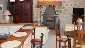 A kitchen with a stone wall, wooden cabinets, a built-in oven, and a dining area with a table and chairs.