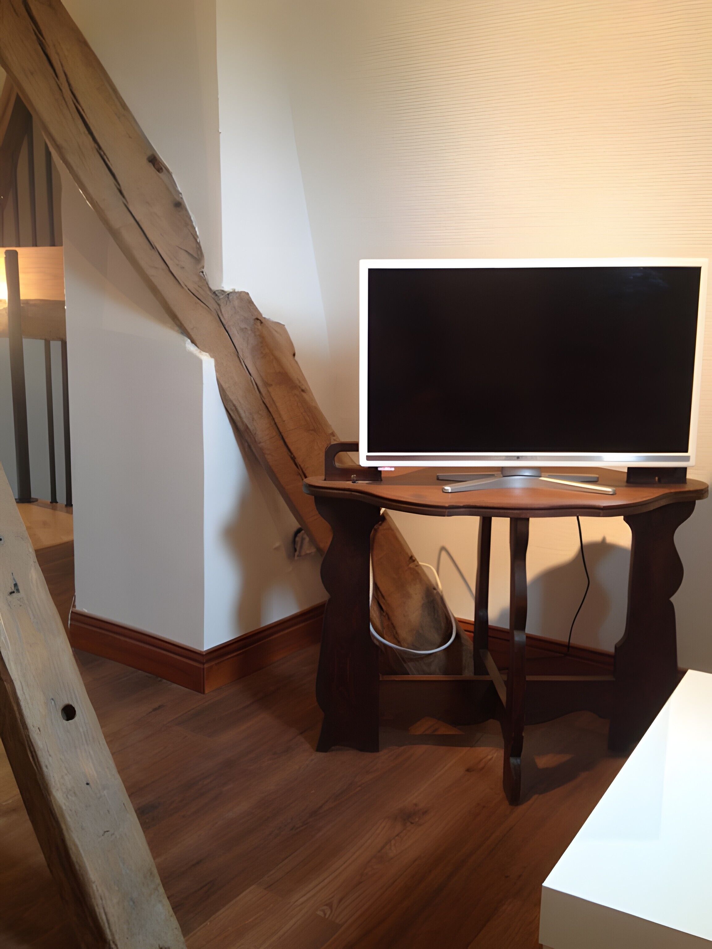 A room with a wooden desk, a flat-screen TV, and a wooden staircase.