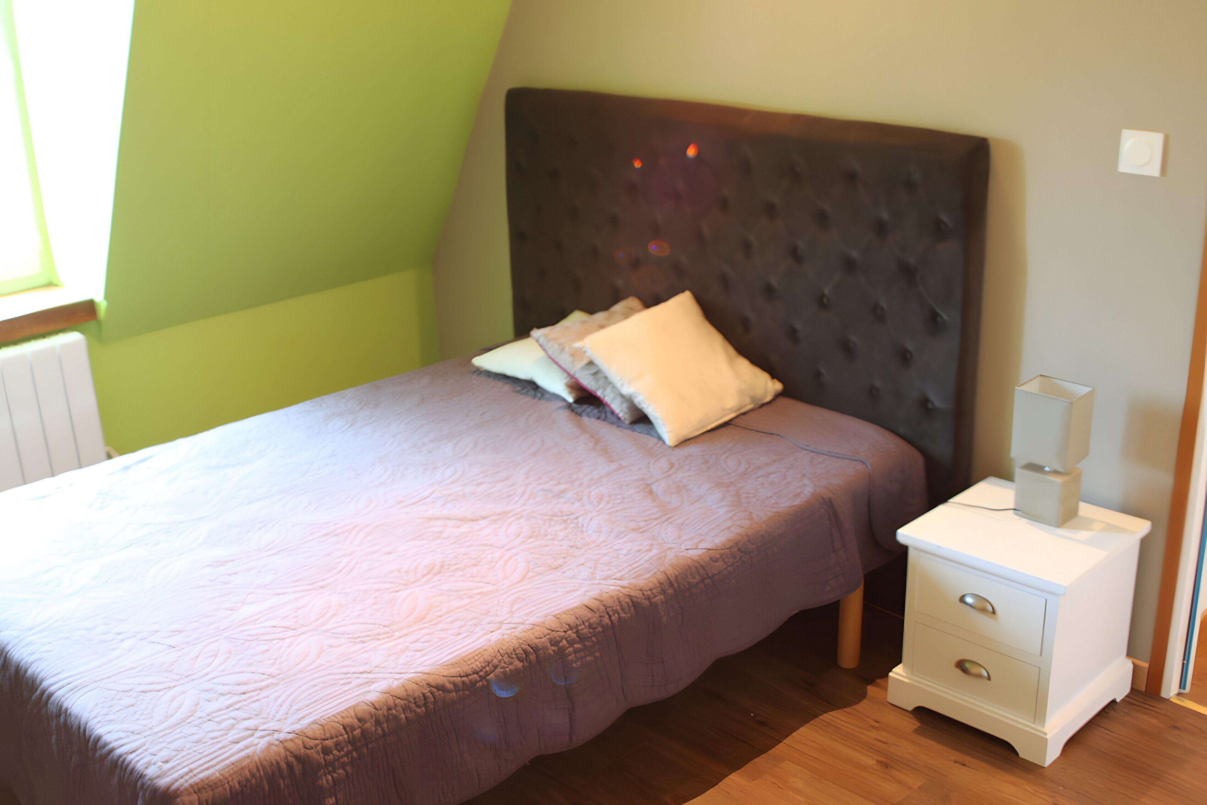 A bedroom with a bed, a nightstand, and a window.
