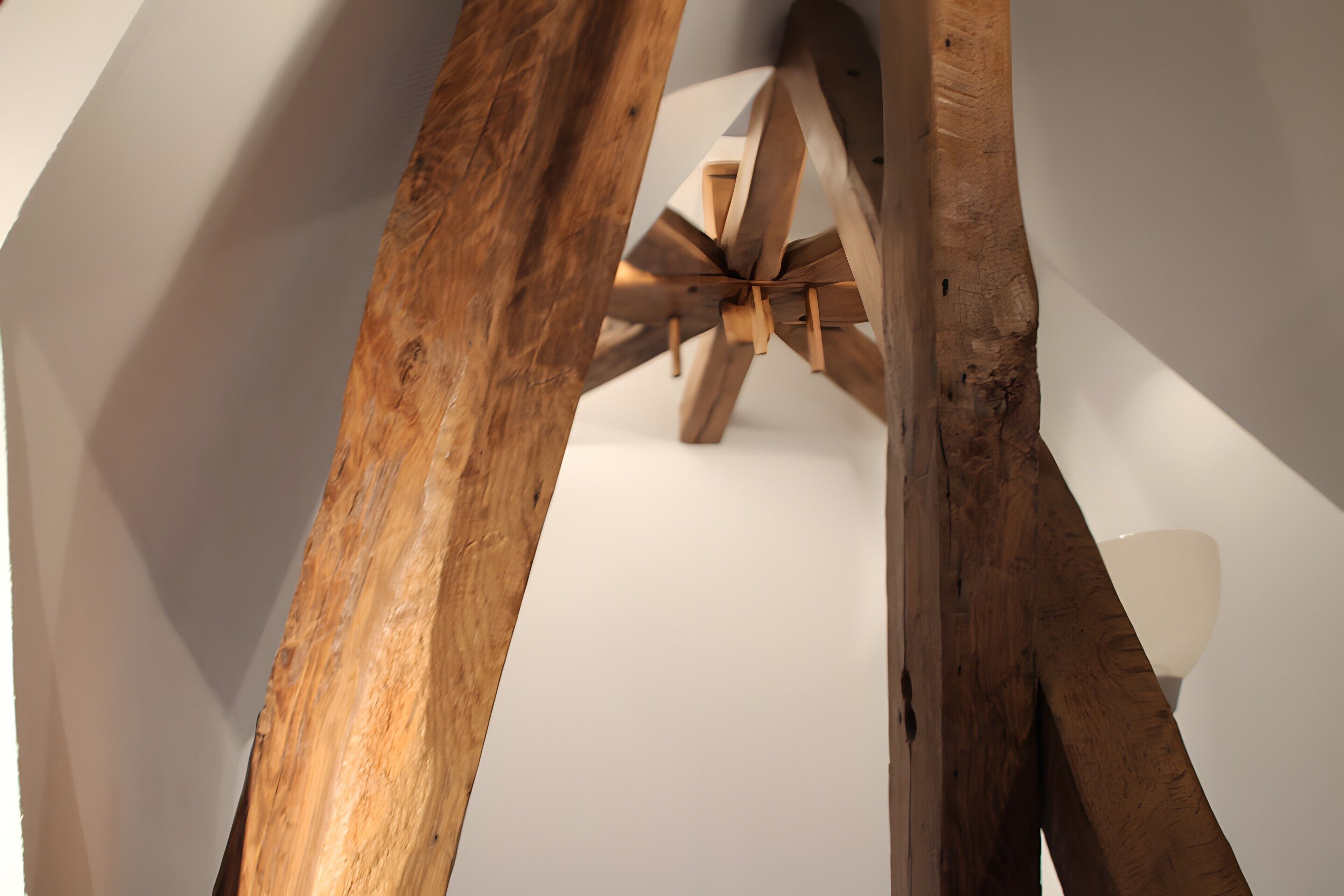 A wooden ceiling structure with beams and a white wall.