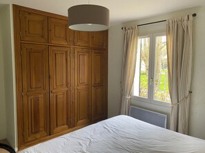 Ein Schlafzimmer mit Bett, Holzschrank, Fenster mit Vorhängen und einer Pendelleuchte.