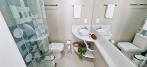 Moderni kylpyhuone, jossa on lasinen suihkuseinä, valkoinen pesuallas peilillä, wc-istuin ja pieni kasvi tasolla.