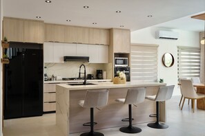 A modern kitchen with a central island, bar stools, a microwave, and a refrigerator.
