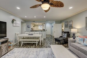 Ein modernes Wohnzimmer mit Essbereich, einer Küche im Hintergrund und einem Deckenventilator mit Blätterdesign.