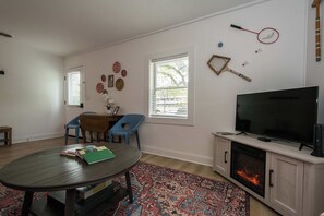 A living room with a TV, fireplace, blue chairs, a table with books, and decorative wall items.