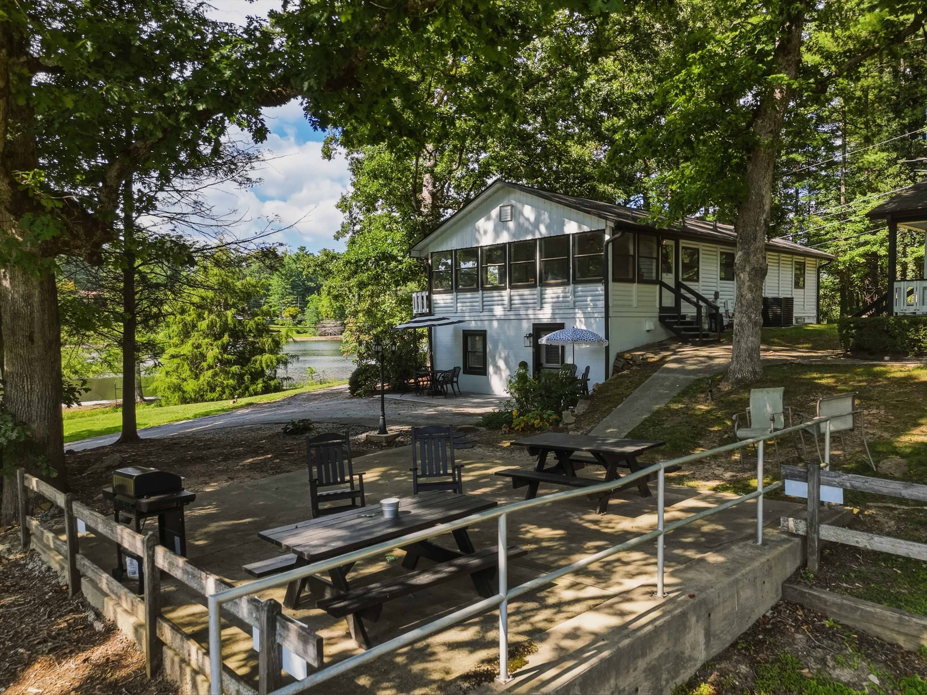 A picnic area with benches and a grill, surrounded by trees and a lake view.