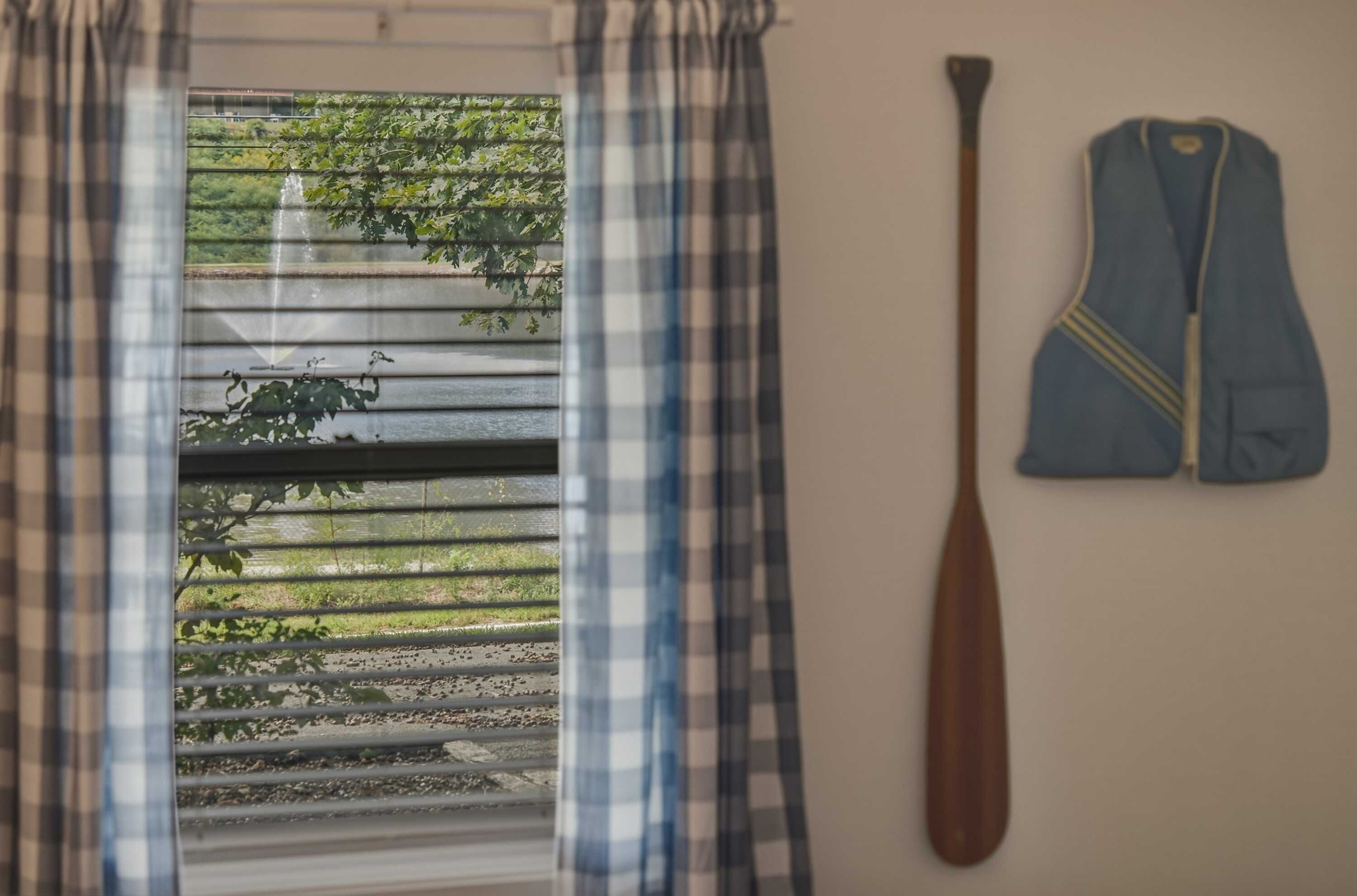 Une fenêtre donnant sur un paysage verdoyant, une batte de baseball en bois et une veste bleue accrochée au mur.