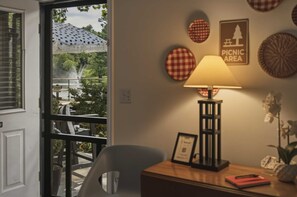 A room with a table lamp, a chair, and a view of an outdoor area with a sign indicating a picnic area.