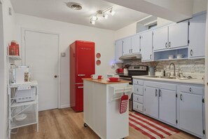 A compact kitchen with white cabinets, a red refrigerator, and a small island with a sink.