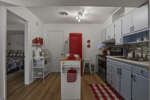 A compact kitchen with white cabinets, a red appliance, and a small dining area.