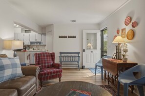 A cozy living room with a red plaid armchair, a blue bench, a wooden coffee table, and a dining area with a blue chair and a lamp.