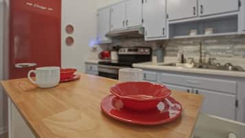 Une cuisine avec un réfrigérateur rouge, des armoires blanches et un plan de travail en bois, sur lequel se trouvent un saladier rouge et une tasse blanche.