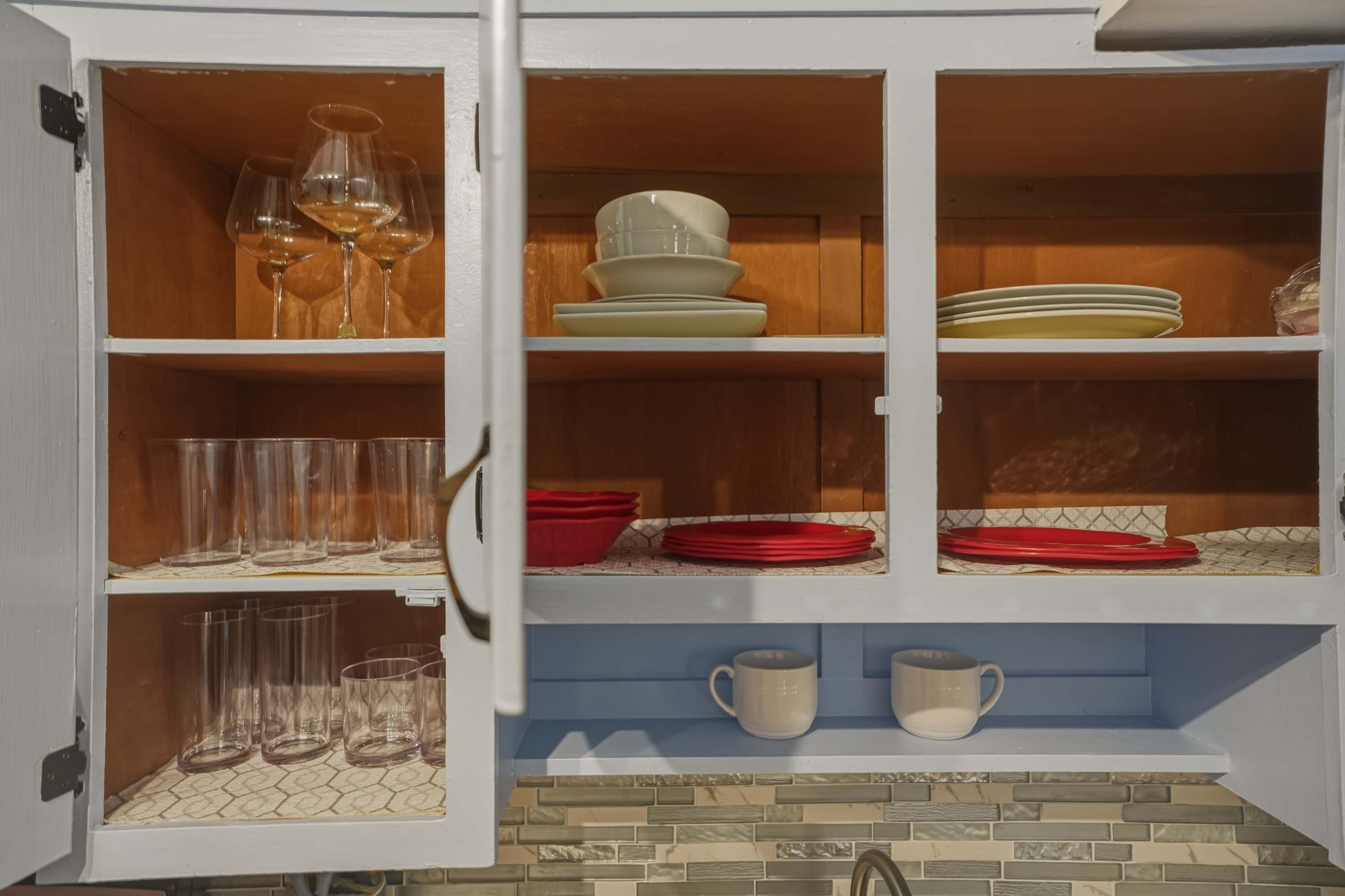 A kitchen cabinet with wine glasses, plates, and cups.
