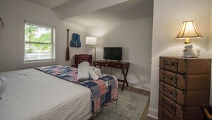 Um quarto com cama, escrivaninha, televisão e cómoda.