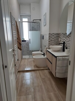 Un baño con ducha, dos inodoros, un lavabo y un espejo.