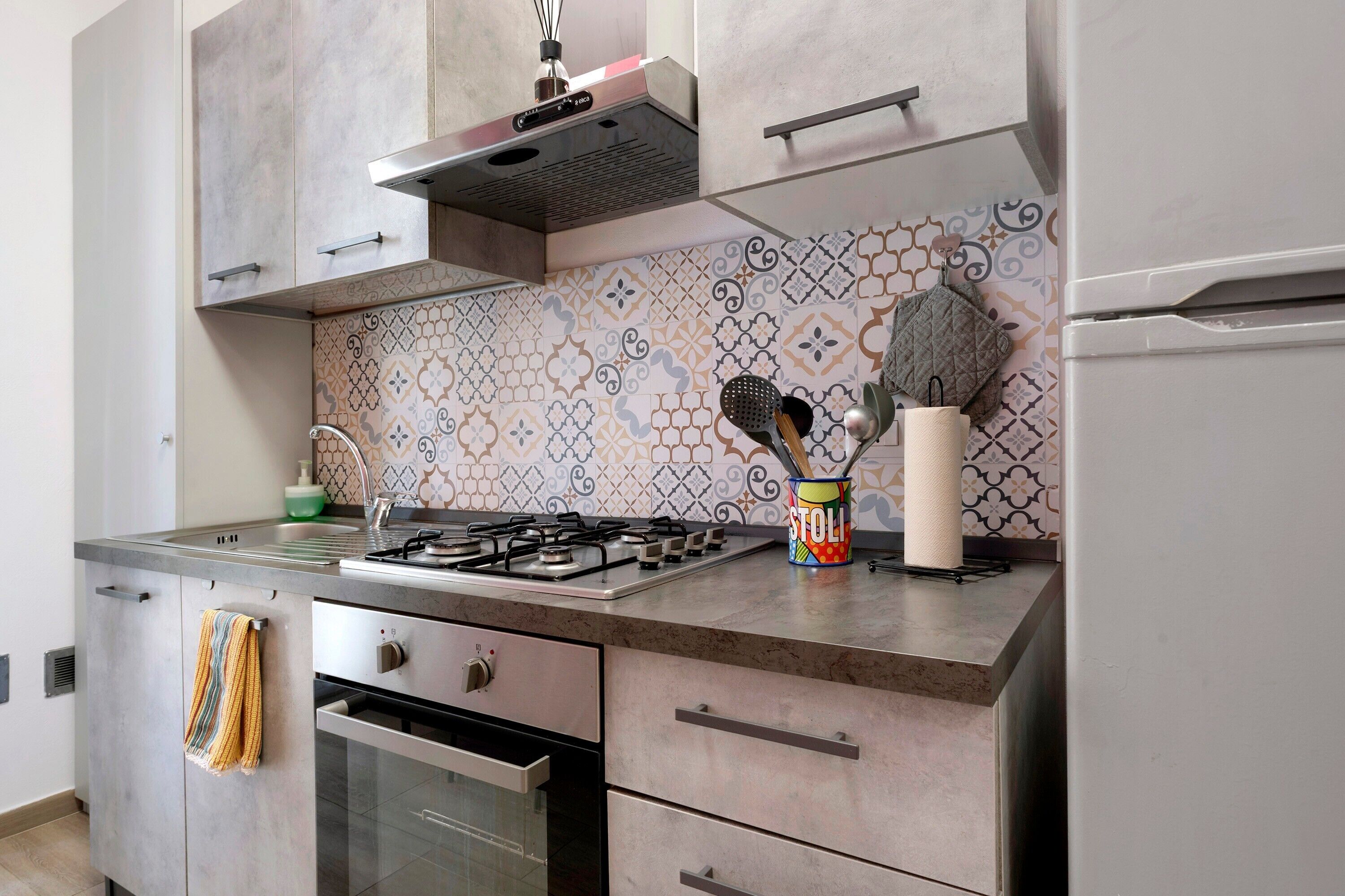Una cucina con piano cottura a gas, forno, pensili in acciaio inossidabile e schienale decorato.