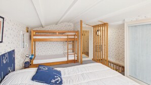 Ein Zimmer mit Etagenbetten, einem Schreibtisch, einem Stuhl, einer Lampe und einem Fenster.