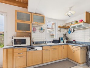 A kitchen with wooden cabinets, a microwave, a sink, and a window. - House for 4, 1 km from beach, garden & BBQ (Les Portes-en-Ré)