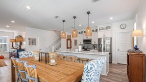 A modern kitchen with white cabinetry, stainless steel appliances, and a wooden dining table with blue patterned chairs. - Fin and Tonic - Private Pool + 6 Bikes (Inlet Beach)