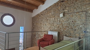 Une pièce avec un mur en pierre, une chaise rouge, un lit recouvert d’une couverture verte et un plafond en bois.