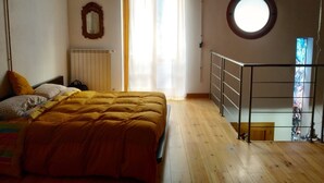 Une chambre à coucher avec un lit, une fenêtre, un radiateur, un miroir et une fenêtre ronde dans le mur.