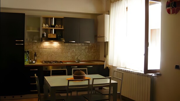 Une cuisine avec une table et des chaises, une fenêtre avec des rideaux et un radiateur.