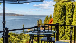 Ett bord med en flaska och glas, ett randigt parasoll och utsikt över havet.