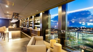 A modern hotel lobby with a bar, seating area, and large windows offering a city view.