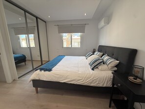 Ein Schlafzimmer mit einem Bett, einem Nachttisch, einem Sessel, einer Schiebetür aus Glas und einem Fenster.