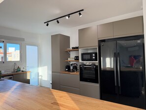 Eine moderne Küche mit integriertem Mikrowellenherd, Backofen und Kühlschrank, einer Holz Arbeitsplatte und einem Fenster mit Blick auf Gebäude.